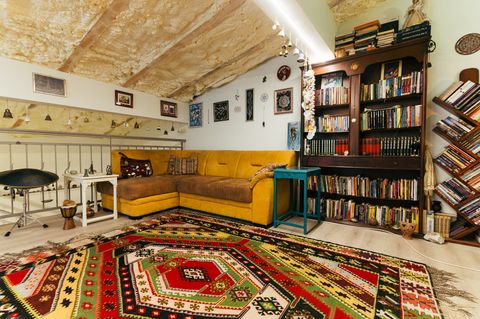 A spacious room with a yellow sofa, a large library and a colourful rug