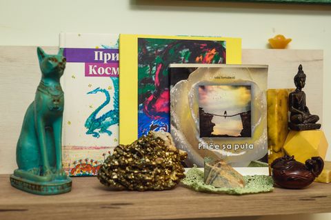 My book “Priče iz Sveta Kosmičke strele” and other books on a shelf among figures and crystals