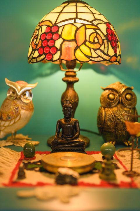 A stained-glass lamp between two owl figures on a green background